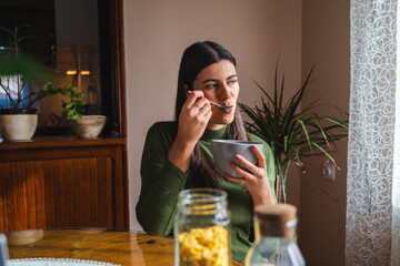 A young woman eating corn flakes for breakfast in the morning in her apartment	