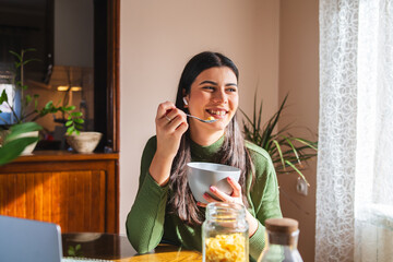 A young woman eating corn flakes for breakfast in the morning in her apartment	