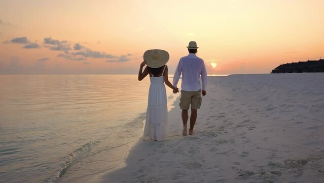 A beautiful couple walks along a tropical beach and watches the sunset in the Maldives islands