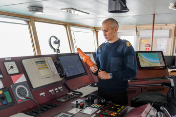 Officer on watch with SART on the navigational bridge. Caucasian man in blue uniform sweater using search and rescue radar transponder on the bridge of cargo ship.