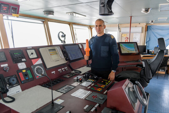 Officer on watch with SART on the navigational bridge. Caucasian man in blue uniform sweater using search and rescue radar transponder on the bridge of cargo ship.