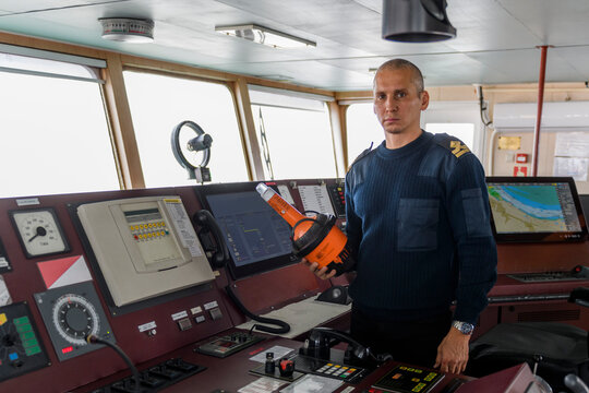 Officer on watch with EPIRB on the navigational bridge. Caucasian man in blue uniform sweater using emergency position indicating radio beacon on the bridge of cargo ship.