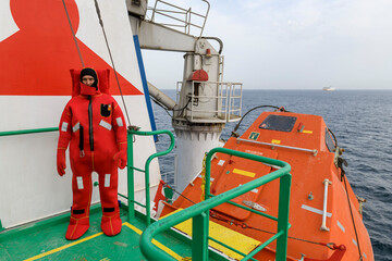 Seaman wearing Immersion Suit on Muster station. Abandon ship drill. Free fall boat. Cargo vessel.