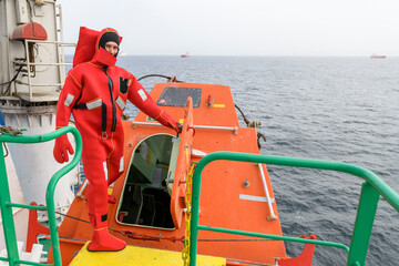 Seaman wearing Immersion Suit on Muster station. Abandon ship drill. Free fall boat. Cargo vessel.