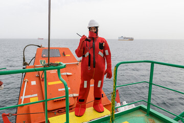 Seaman wearing Immersion Suit on Muster station. Abandon ship drill. Free fall boat. Cargo vessel.