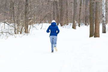 Fototapeta na wymiar An unrecognizable young beautiful athletic girl jogs along a path in the winter forest