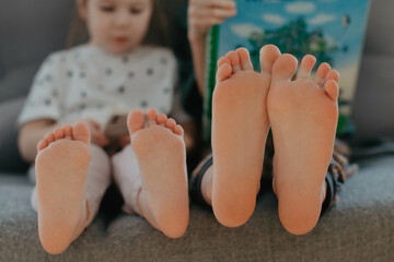 Big brother and little sister holding bare feet close up to camera . Blurred face on background 