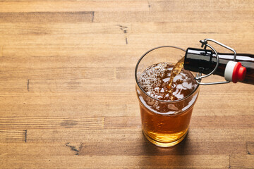 Pouring beer into pint glass on a wooden table - obrazy, fototapety, plakaty