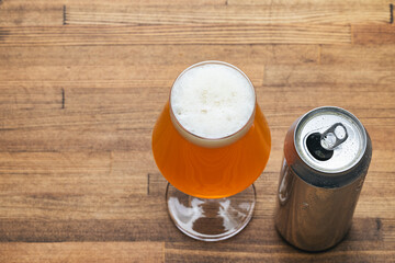 Craft beer glass with open can on wooden table