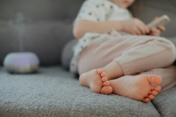 little girl holding bare feet close up to camera and watching phone . Blurred face on background....