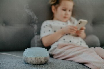 little girl holding bare feet close up to camera and watching phone . Blurred face on background. Diffuser with essential oil 