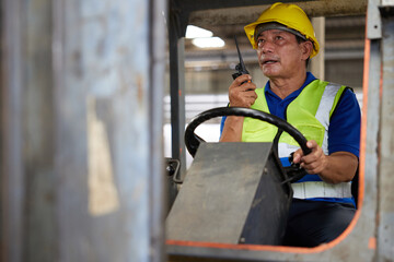 senior worker using walkie talkie and holding steering wheel on forklift truck in the factory