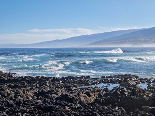 Rocky shore and natural pools of Tenerife coast, with white rolling waves of the sea breaking