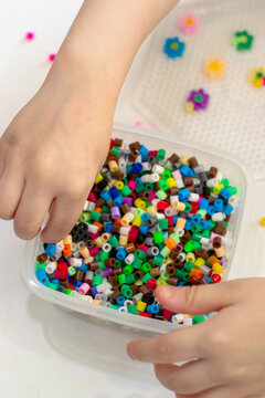 Close-up of children's hands sorting perler beads in a container, multi-colored meltable mosaic