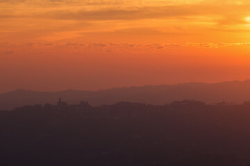 pink sunrise sky with the silhouette of an italian village on the top of a hill in Piedmont