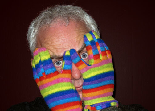 Portrait of a man wearing striped multi coloured gloves holding his hands in front of his face