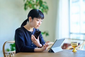 タブレットpcとスマートフォンを見比べる若い女性