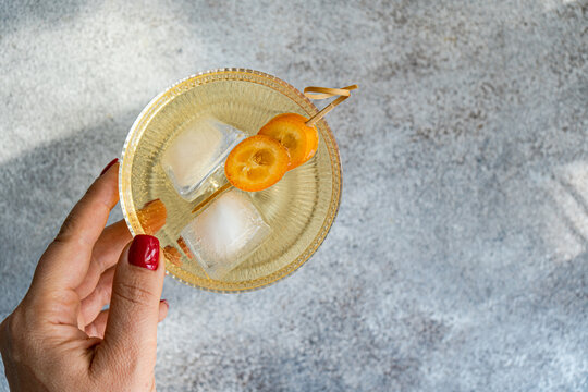 Overhead view of a woman reaching for a vodka tonic cocktail with kumquat garnish