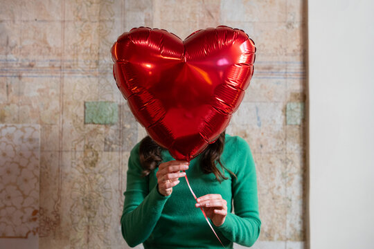 Woman holding a red heart shaped balloon in front of her face