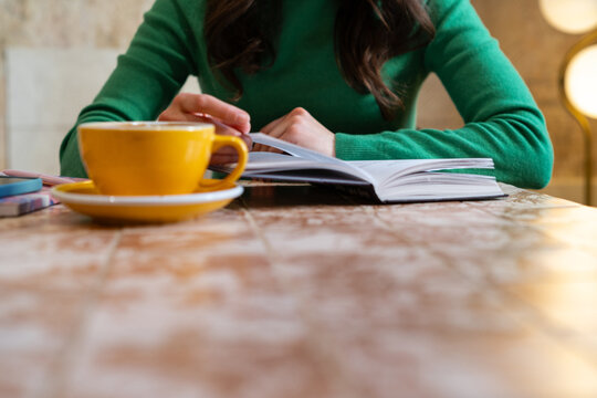 Woman sitting at a table with a hot drink reading a book