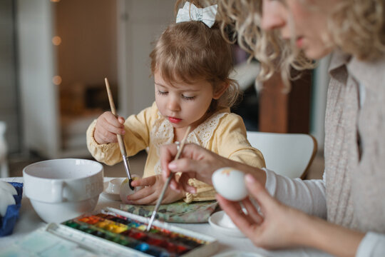 Close-up of a mother and daughter sitting at a dining table decorating Easter eggs