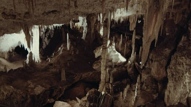 Interior of a vast limestone cave is adorned with geological formations including stalactites hanging from the ceiling and stalagmites rising from the ground