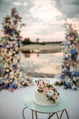 wedding cake decorated with roses at sunset near the water and against the backdrop of the wedding arch