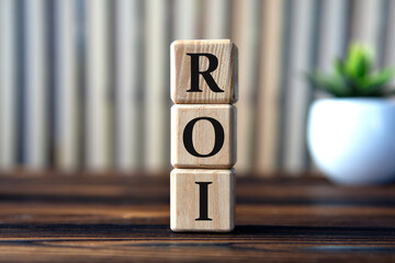 ROI - acronym on wooden cubes on the background of books and a cactus