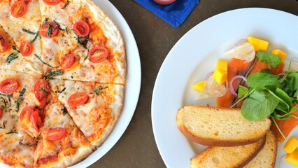 Italian cuisine experience showing delectable cheese pizza with ripe tomatoes, fresh salad with smoked salmon and mangoes, emphasizing Mediterranean diet benefits. Balanced meal and culinary delight.