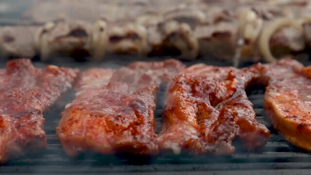 Food preparation process of marinated and spiced pork fillet meat cooked on charcoal barbeque grill. Outdoors cooking.