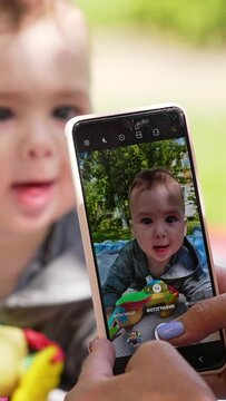 Mother wants to take photos of her son. Little boy wants to take the phone ignoring toys. Blurred backdrop. Vertical video.