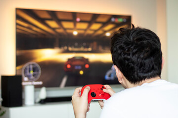 Young man playing car race game using video games console on television. Gamer with wireless...