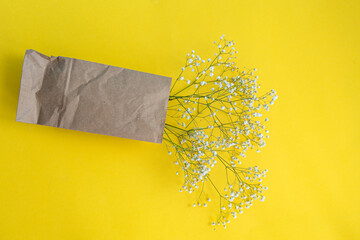 A bouquet of white small gypsophila flowers in eco-packaging lies on a yellow table.