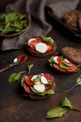 Rye bun sandwiches or burgers with salami, mozzarella, cherry tomatoes, chard leaves and ketchup on dark concrete background. Side view