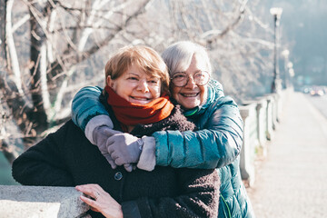 Happy couple of elderly women meet and embrace each other in the park, two senior friends or family members stay together expressing love and tenderness