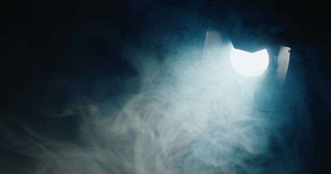 In the darkness, a potent directional light pierces through, illuminating swirling fog within its beam.