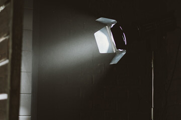 A single studio light shines brightly, casting a beam across the dark ambiance of a brick-walled...