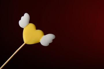 One yellow heart-shaped lollipop with wings on a dark red background. Love. Horizontal banner for Valentine's Day.