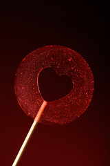A round transparent red lollipop on a dark red background. Love. Vertical banner for Valentine's Day.