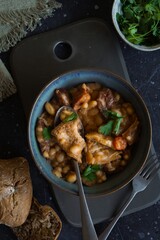 Tripas - pork tripe stew with white beans and smoked sausages with bread and coriander on the dark table. Flat lay
