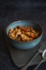 Pork tripe stew with white beans and smoked sausages in a blue bowl on the dark table with copy space