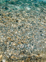 Close up sea waves stones shells beach summer day. top view above transparent water.
