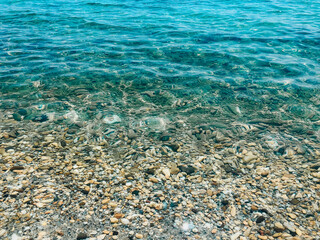 Naklejka na ściany i meble Close up sea waves stones shells beach summer day. top view above transparent water.