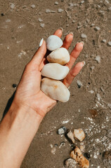 Woman hand manicure holding white beautiful stones above sea sandy summer beach.