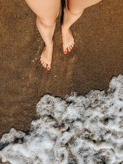 Woman legs barefoot at sea foam waves on sand beach summer day. top view above women feet.