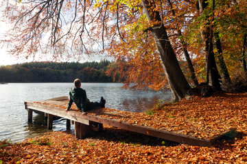 Mann sitz entspannt am Steg am See im Herbst, Seele baumeln lassen