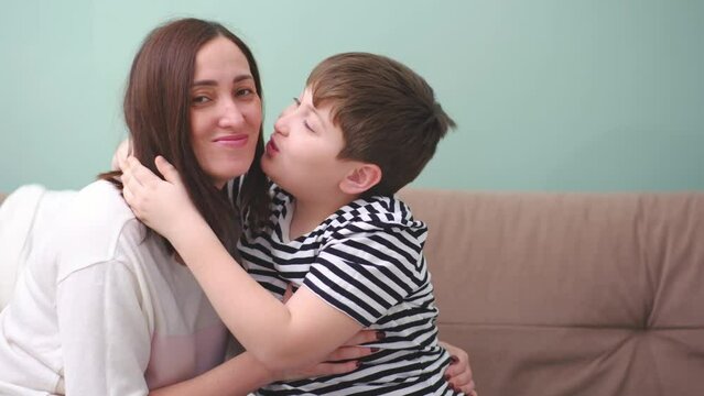 Cute son kisses mom. Happy little boy hugging his mother at home. Loving mum and kid cuddling embrace cheerful to family holiday event.Concept love mom.