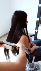 Planchado de cabello a mujer joven clienta con plancha de pelo y peine alisador con cepillo doble en Salón de Belleza. Alisado de cabello y peluquería profesional. 