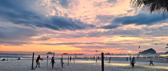 Sunset with people playing volleyball and beach tennis on Leme beach. Nature. Open air. Sports. Rio...