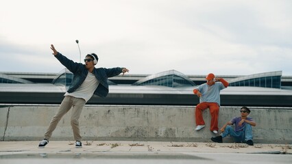 Handsome break dancer enjoy perform freestyle movement with asian friend cheering behind. Hipster...
